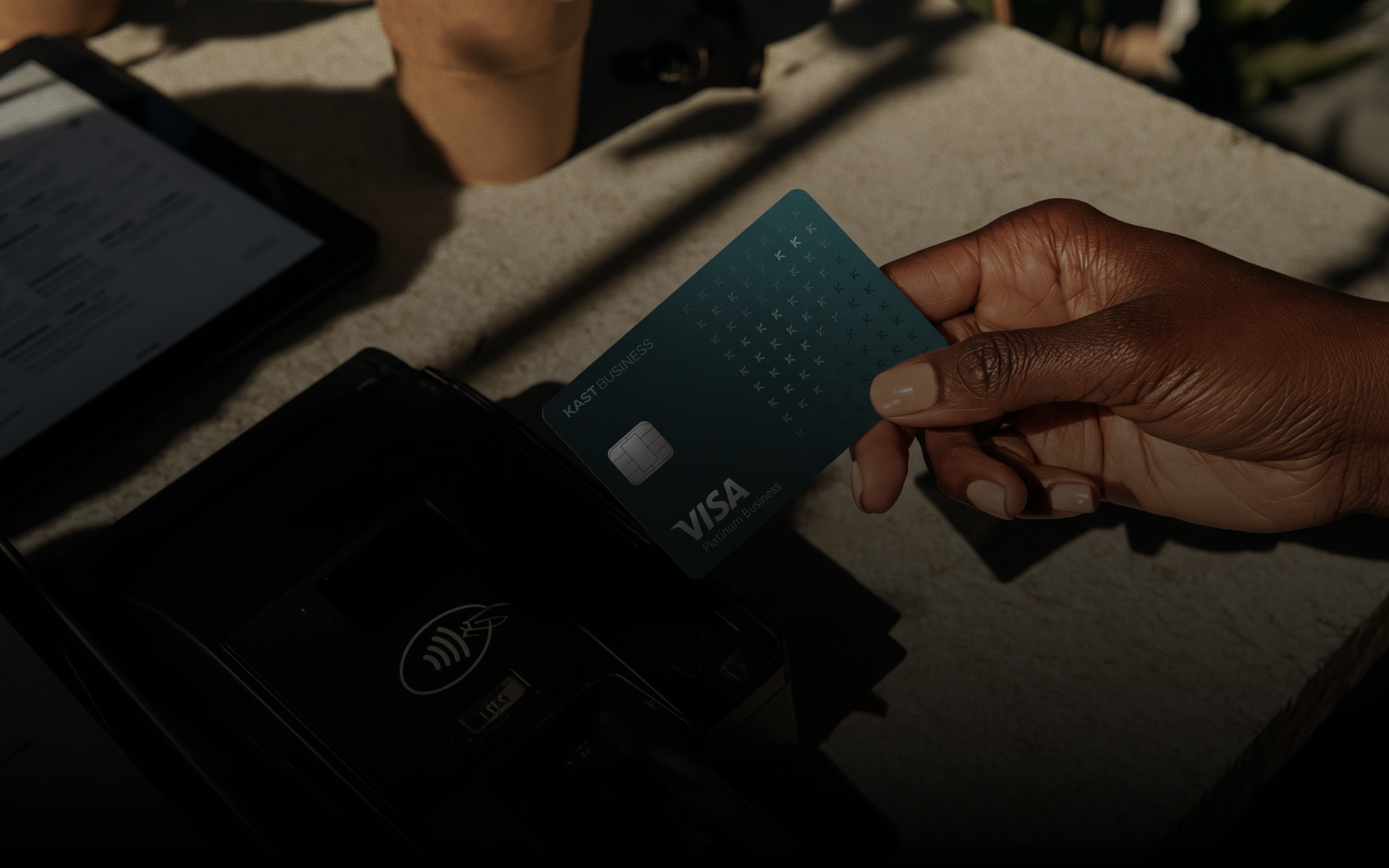 Uma mão segura um cartão Visa da KAST Business sobre uma maquininha por aproximação.